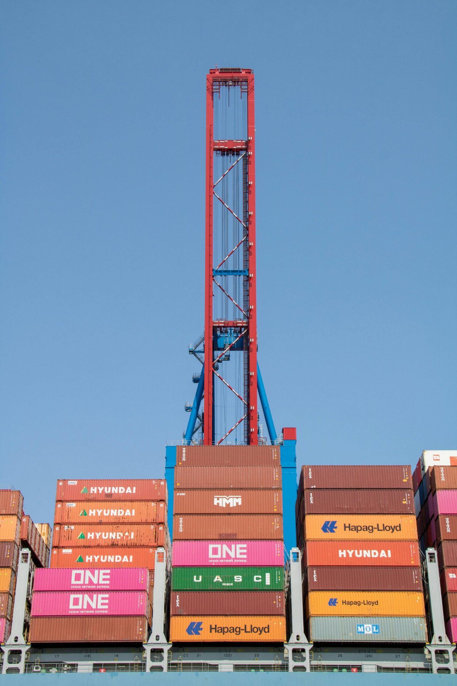 Vertical view of stacked cargo containers under a tall crane at Hamburg port.