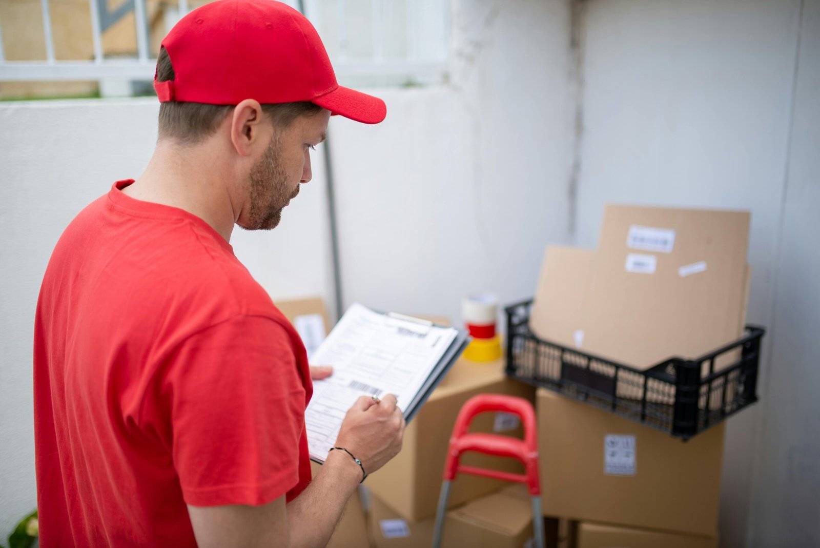 Delivery person in red uniform checks packages. Outdoor location, Portugal.