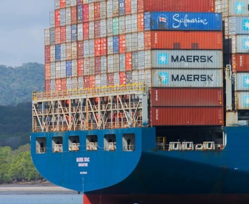 A cargo ship loaded with containers navigates the Panama Canal under clear skies.